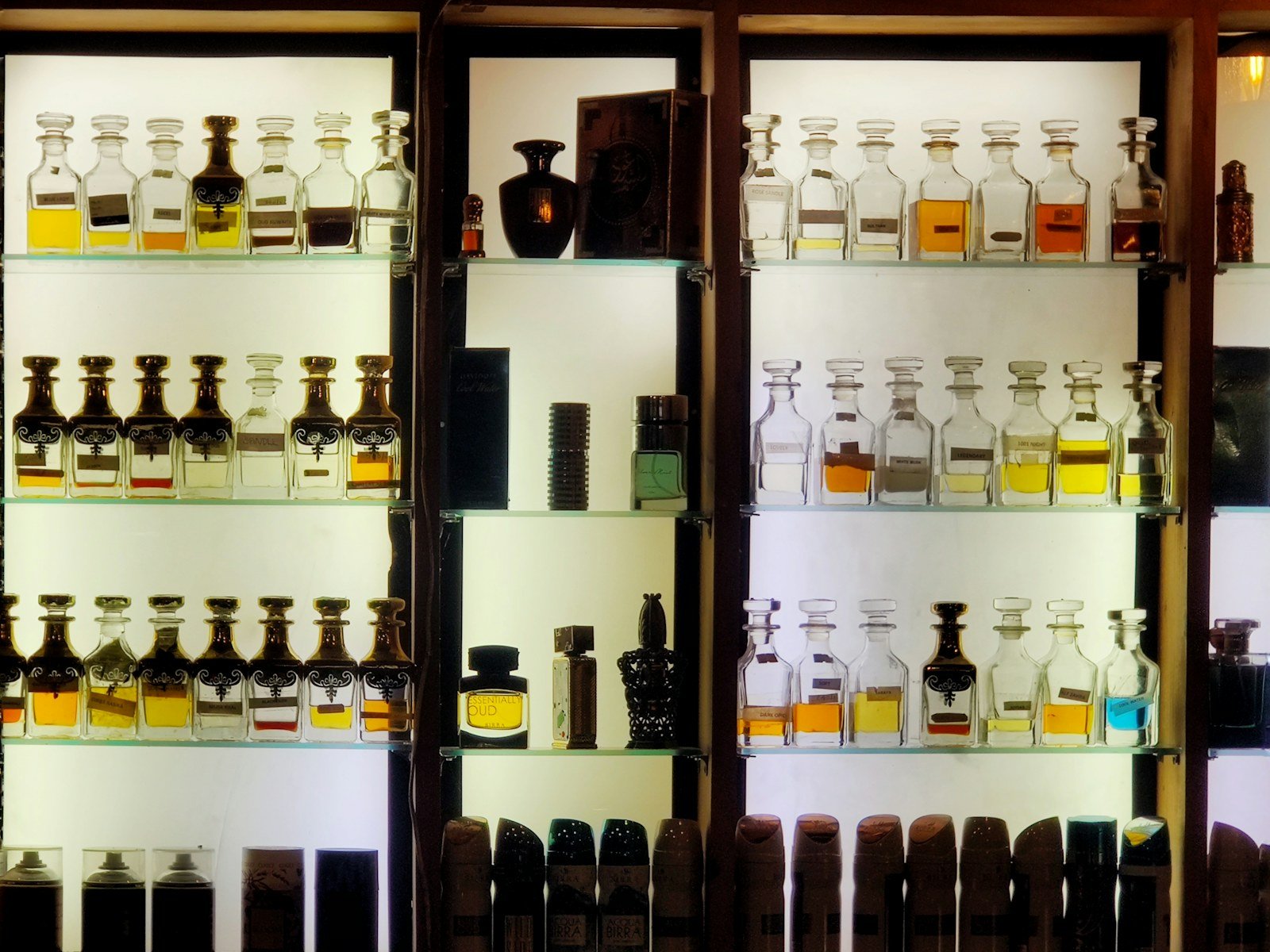 Rak kayu berlampu berisi deretan botol parfum attar berbagai warna