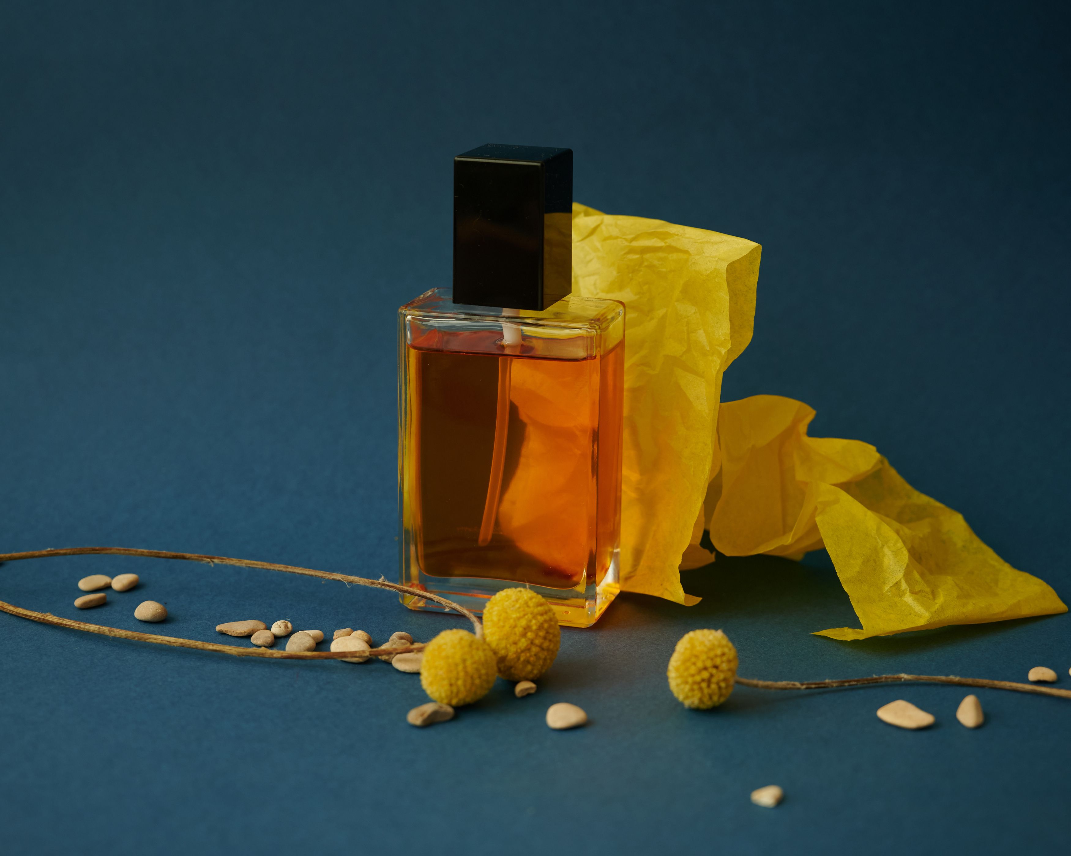 Botol parfum kaca dalam komposisi kertas kuning dan aksen bunga