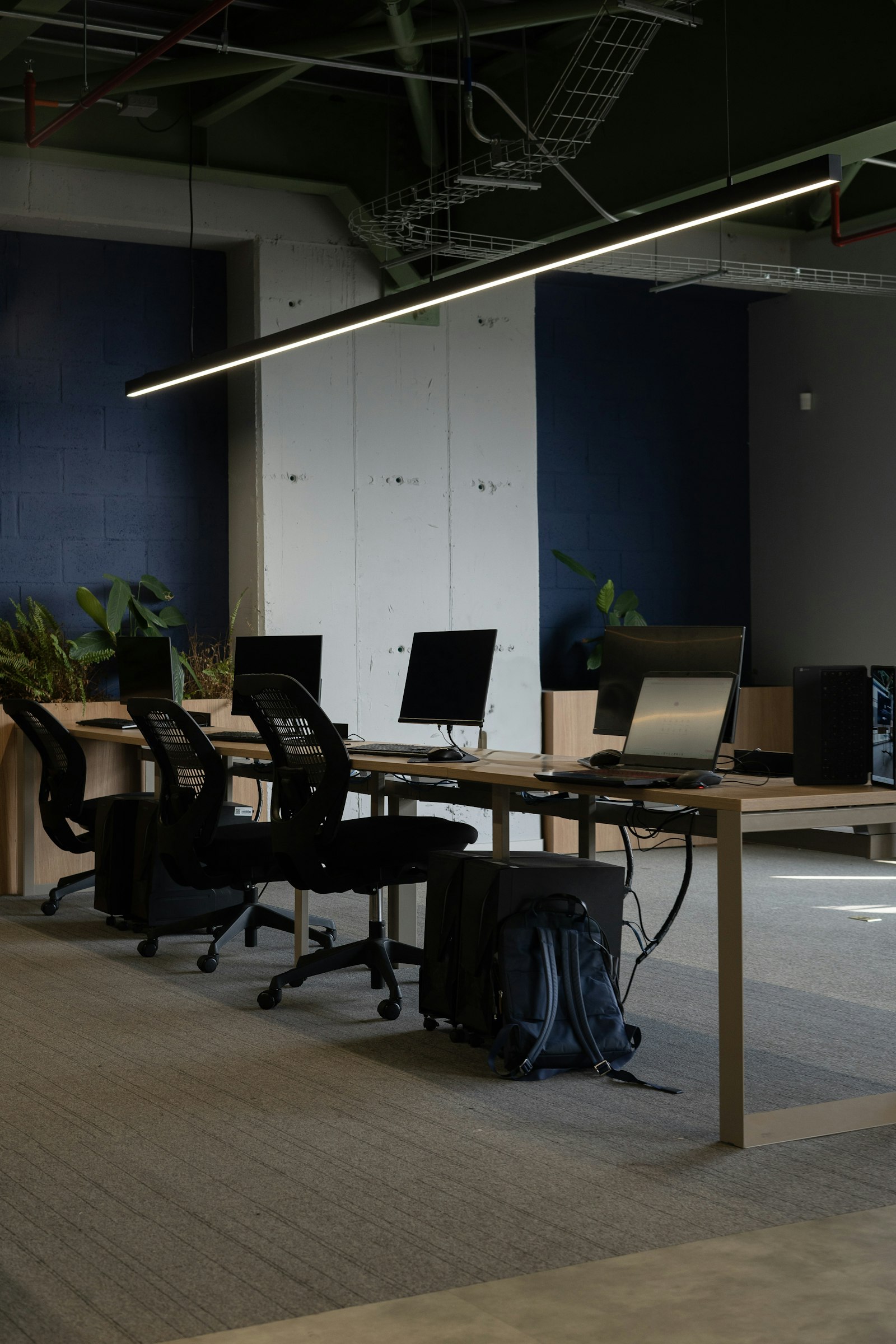 Ruang kerja bersama dengan meja panjang, komputer, dan kursi kantor tanpa orang