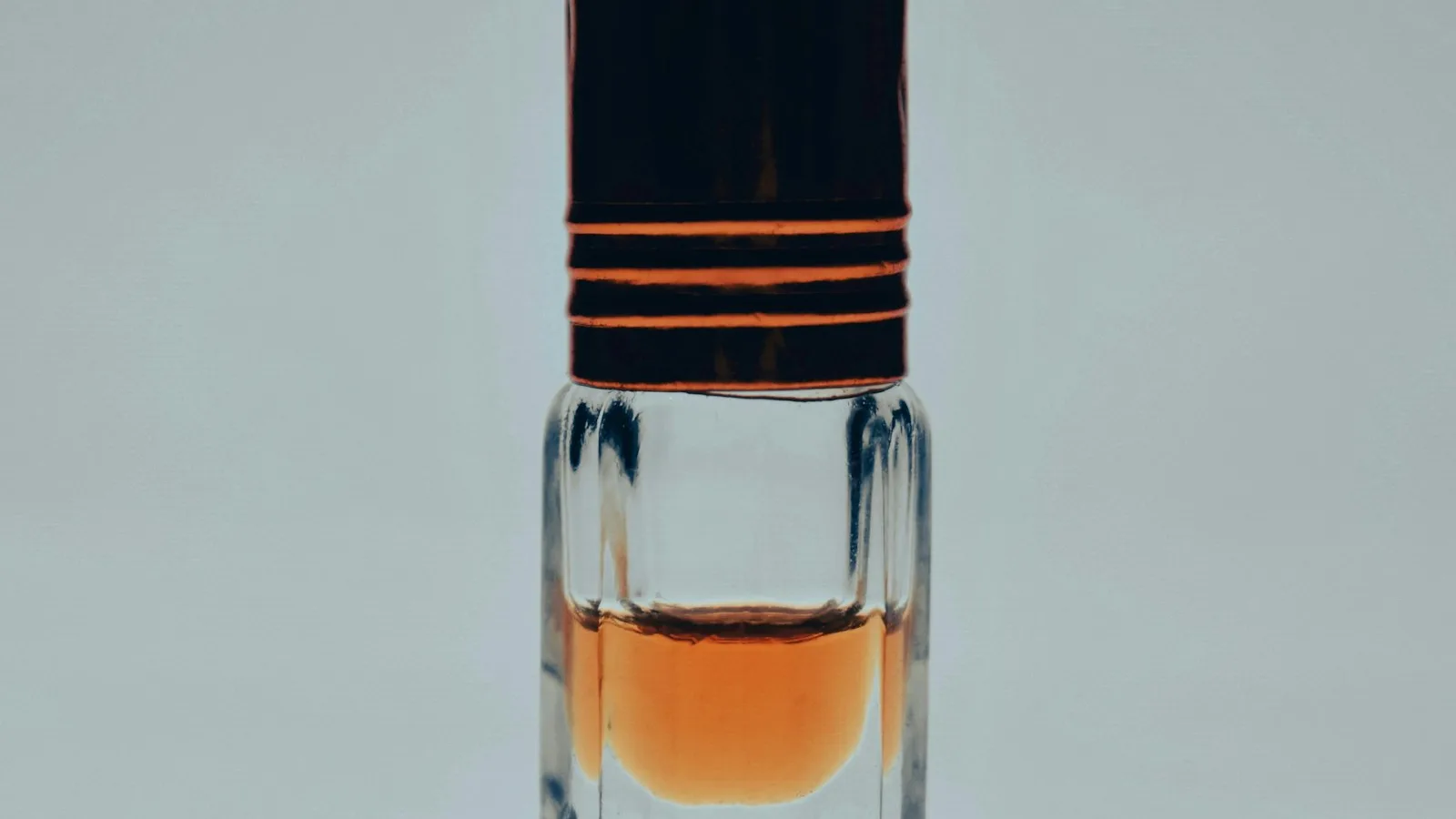 Botol attar kecil bertutup hitam berisi minyak parfum berwarna amber