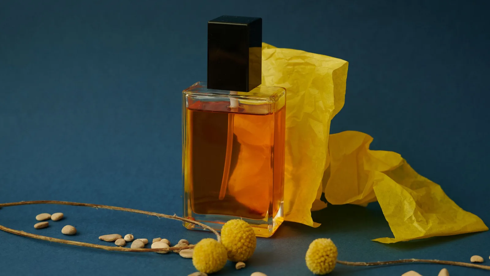 Botol parfum kaca dalam komposisi kertas kuning dan aksen bunga