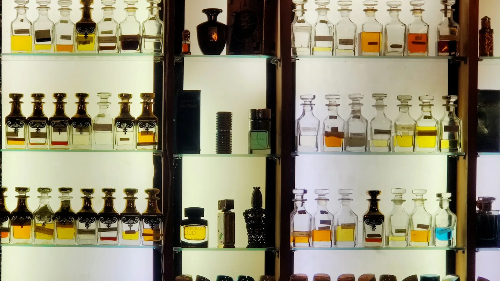Rak kayu berlampu berisi deretan botol parfum attar berbagai warna
