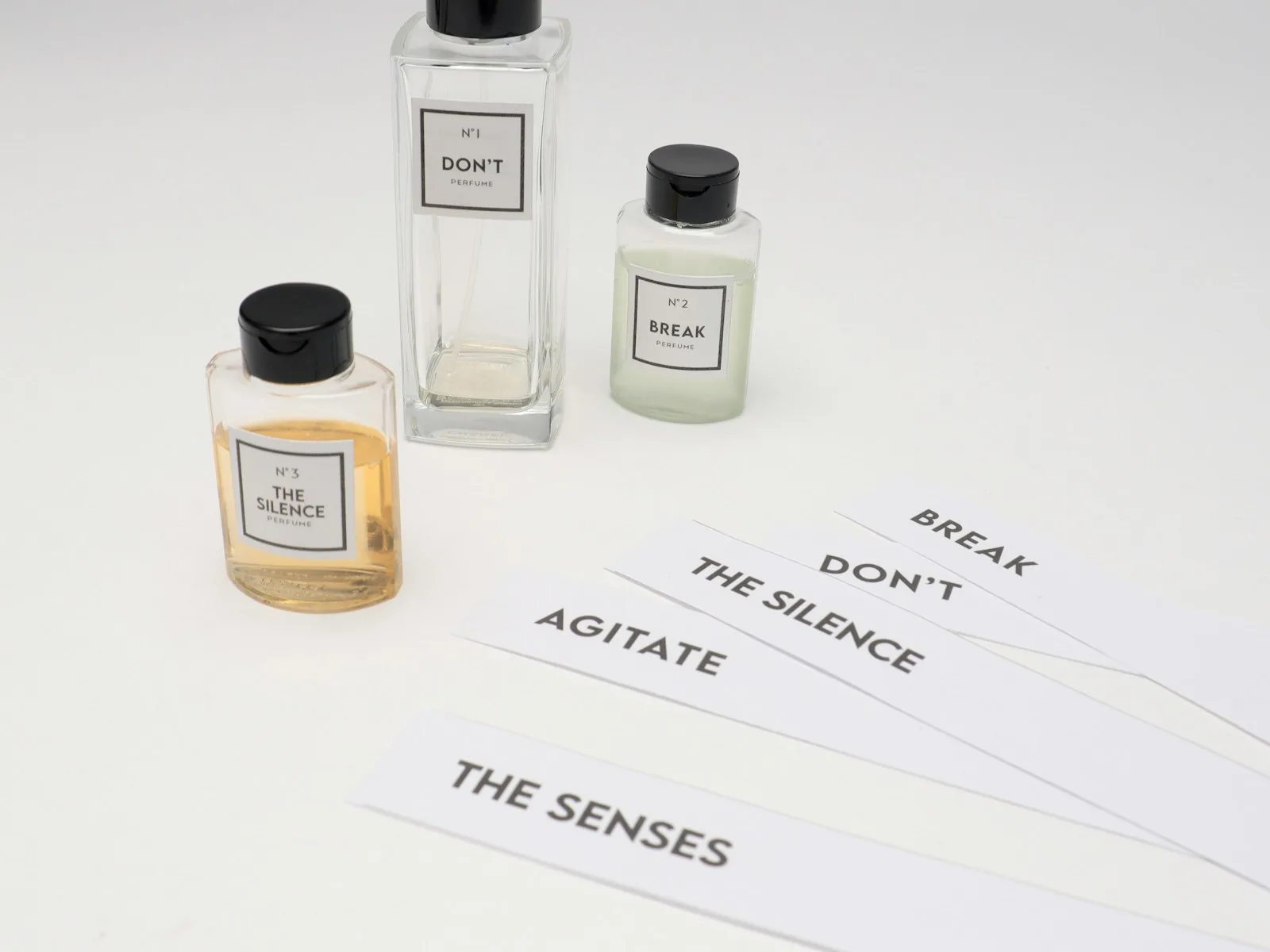 Tiga botol parfum kecil di meja putih dengan beberapa kertas tester berlabel